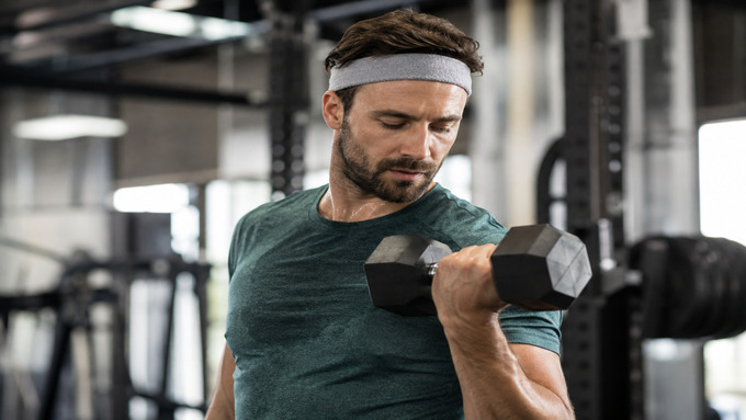 Man wearing a sweatband while lifting a dumbbell in the gym